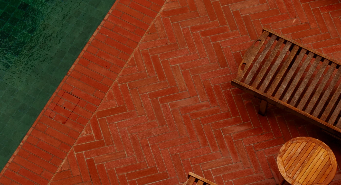 Warm brick pavers in herringbone bond under teak loungers at a pool edge