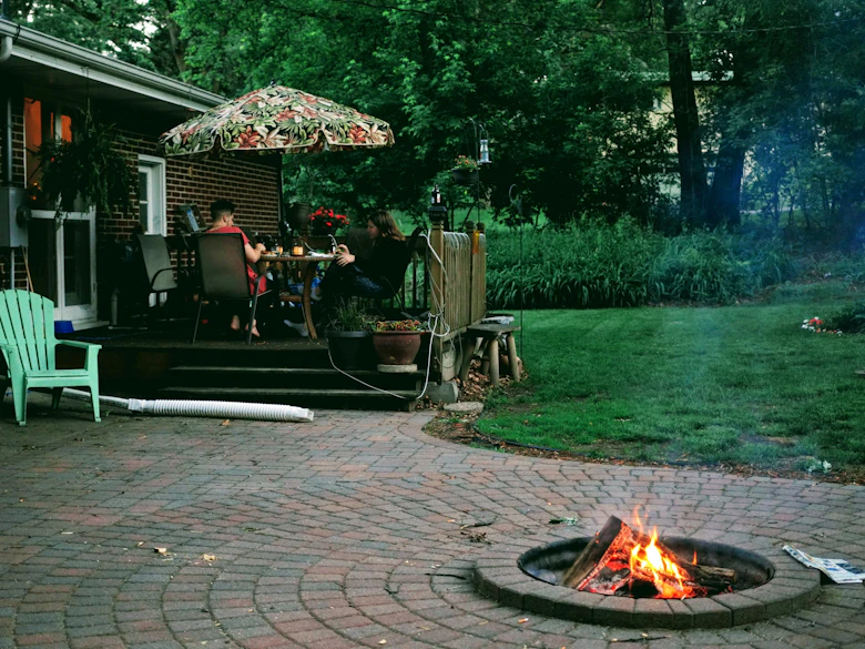Brick-paver patio with a built-in fire pit ring curving past a backyard seating deck